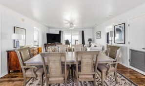 Une salle à manger avec une grande table et des chaises, un téléviseur et une vue sur l’extérieur.