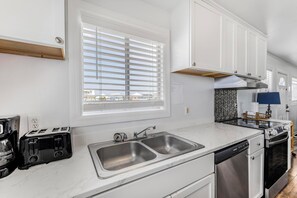 A modern kitchen with a double sink, a toaster, and a dishwasher. - 🏖️ Beachfront Salt and Grace: Direct Gulf Access + Balcony + Dog Friendly (Fort Morgan)