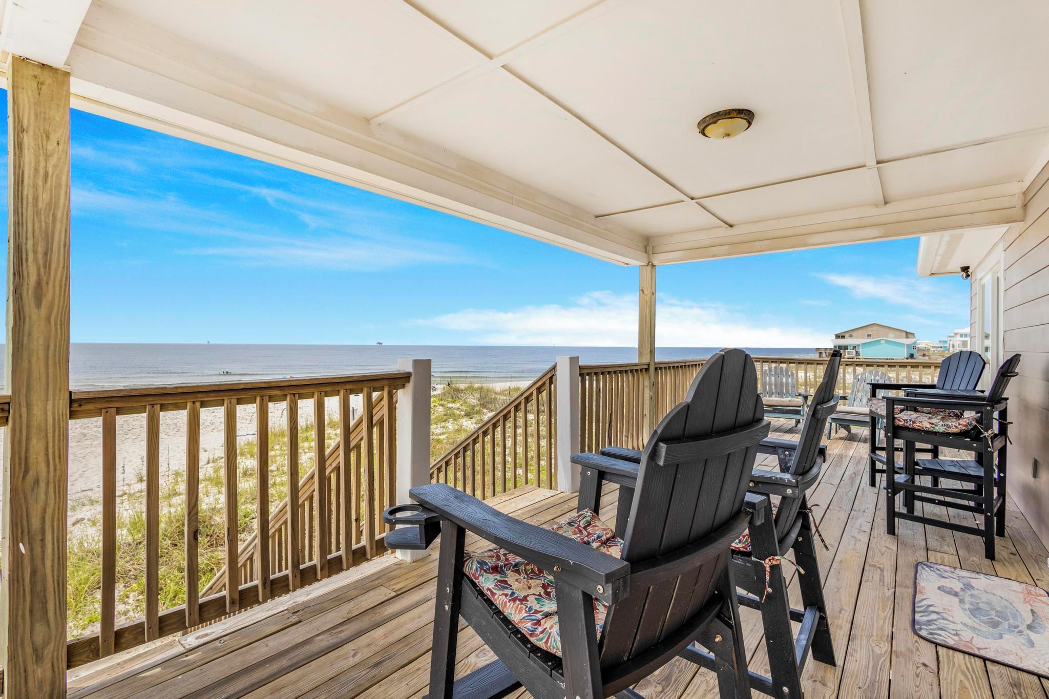Eine überdachte Terrasse im Freien mit Holzgeländern, Blick auf den Strand und mehreren Adirondack-Stühlen.