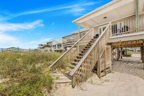 A beachfront property with a wooden staircase leading to a balcony, surrounded by sand and vegetation. - 🏖️ Beachfront Salt and Grace: Direct Gulf Access + Balcony + Dog Friendly (Fort Morgan)