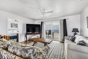 A modern living room with a sofa, a coffee table, a TV, and a view of the beach through the glass door. - 🏖️ Beachfront Salt and Grace: Direct Gulf Access + Balcony + Dog Friendly (Fort Morgan)