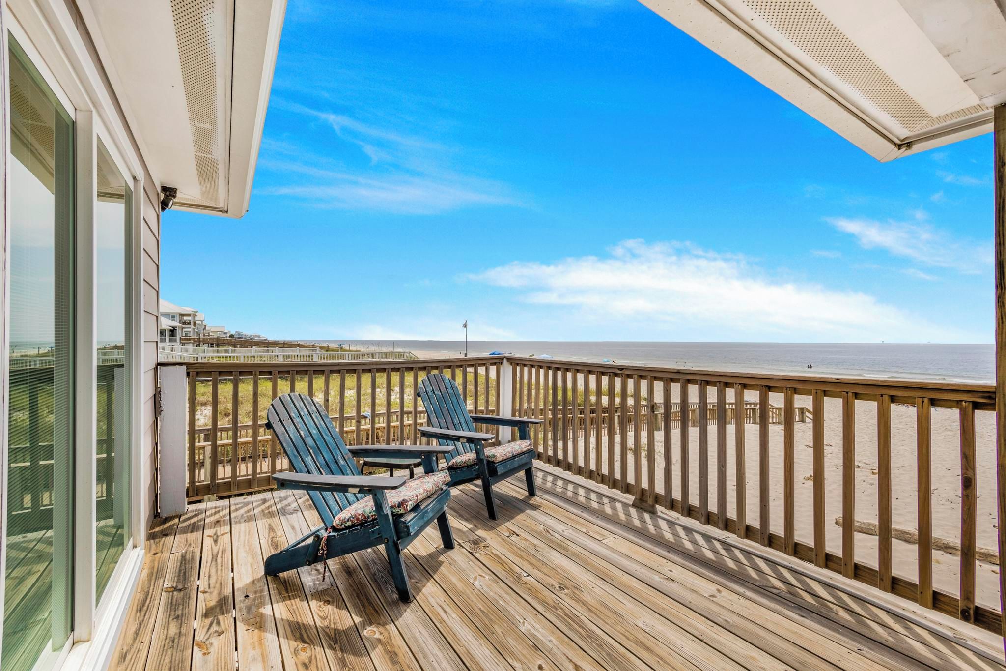 A wooden deck with two Adirondack chairs and a view of the beach.