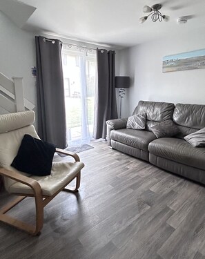 A modern living room with a leather sofa, a wooden chair, and a floor lamp. - Cosy, Comfortable 3bd holiday cottage set on Tolroy, Hayle. (Tolroy Manor Hayle)