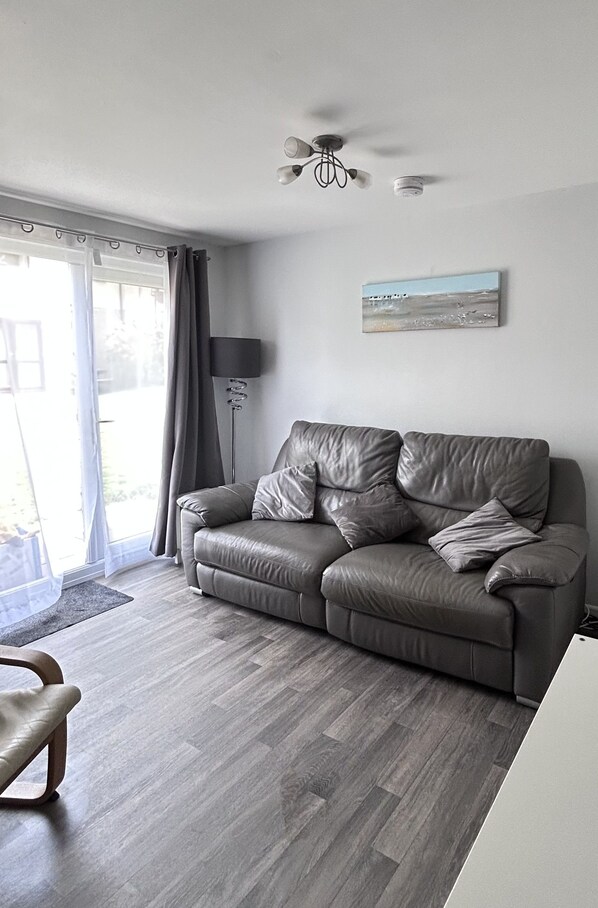 A modern living room with a grey leather sofa, a floor lamp, and a painting on the wall.