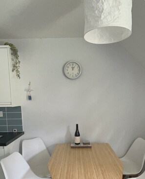 A dining area with a wooden table, white chairs, a wall clock, and a hanging light fixture. - Cosy, Comfortable 3bd holiday cottage set on Tolroy, Hayle. (Tolroy Manor Hayle)