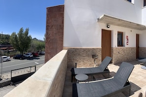 Ein Balkon mit Gartenmöbeln, einem Feuerlöscher und Blick auf parkende Autos und Bäume.