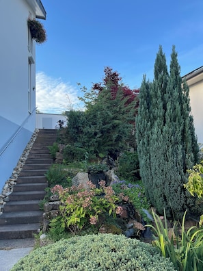 A staircase leading to a building with a white exterior, surrounded by lush greenery and a variety of plants. - Peaceful premium flat (140 sq m), garden, sauna, near Europark and Black Forest (Ettenheim)