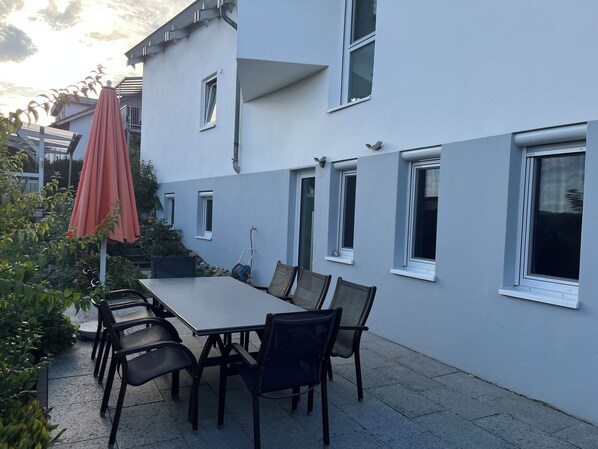 A patio with a table and chairs, a red umbrella, and a building with multiple windows. - Peaceful premium flat (140 sq m), garden, sauna, near Europark and Black Forest (Ettenheim)