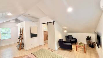 Amplio dormitorio tipo loft con un gran ventanal, una cama, un escritorio, una silla y una planta en maceta.
