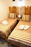 Habitación de hotel con dos camas, cada una con ropa de cama y almohadas a rayas, una mesita de noche con lámpara y cabecera de madera.