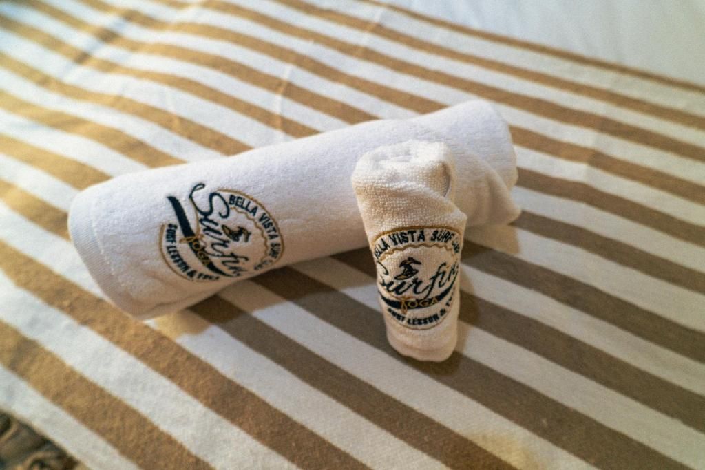A rolled-up towel and a sock with 'Bella Vista' and 'Yoga' text on a striped bedspread.