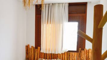 Un dormitorio con cabecera de madera, una cama con ropa de cama estampada, una mesita de noche con lámpara y una ventana con cortinas.