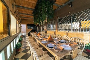 Una larga mesa de comedor con sillas, piso a cuadros y plantas colgantes.