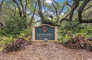 A sign for Sandcastles Villas 200-254, surrounded by lush greenery and trees.