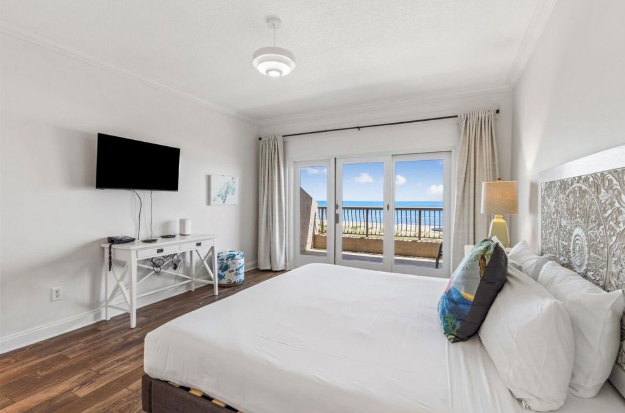 Habitación de hotel con cama, escritorio, televisor de pantalla plana, ventana con vista al mar y balcón.