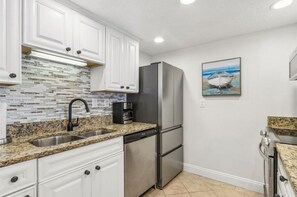 A kitchen with white cabinets, a stainless steel refrigerator, a coffee maker, and a tiled backsplash.
