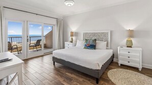 Ein Schlafzimmer mit Bett, Nachttischen, einem Schreibtisch und Blick auf den Strand durch eine Schiebetür.
