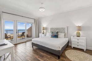 Une chambre à coucher comprenant un lit, des tables de chevet, une commode, un bureau et une vue sur la plage, accessible par une porte coulissante.