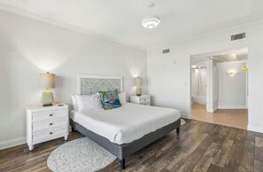 A bedroom with a bed, nightstands, a lamp, a rug, and a door leading to another room.