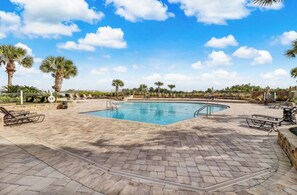 Une piscine dotée d’une terrasse carrelée, entourée de palmiers et de chaises longues.