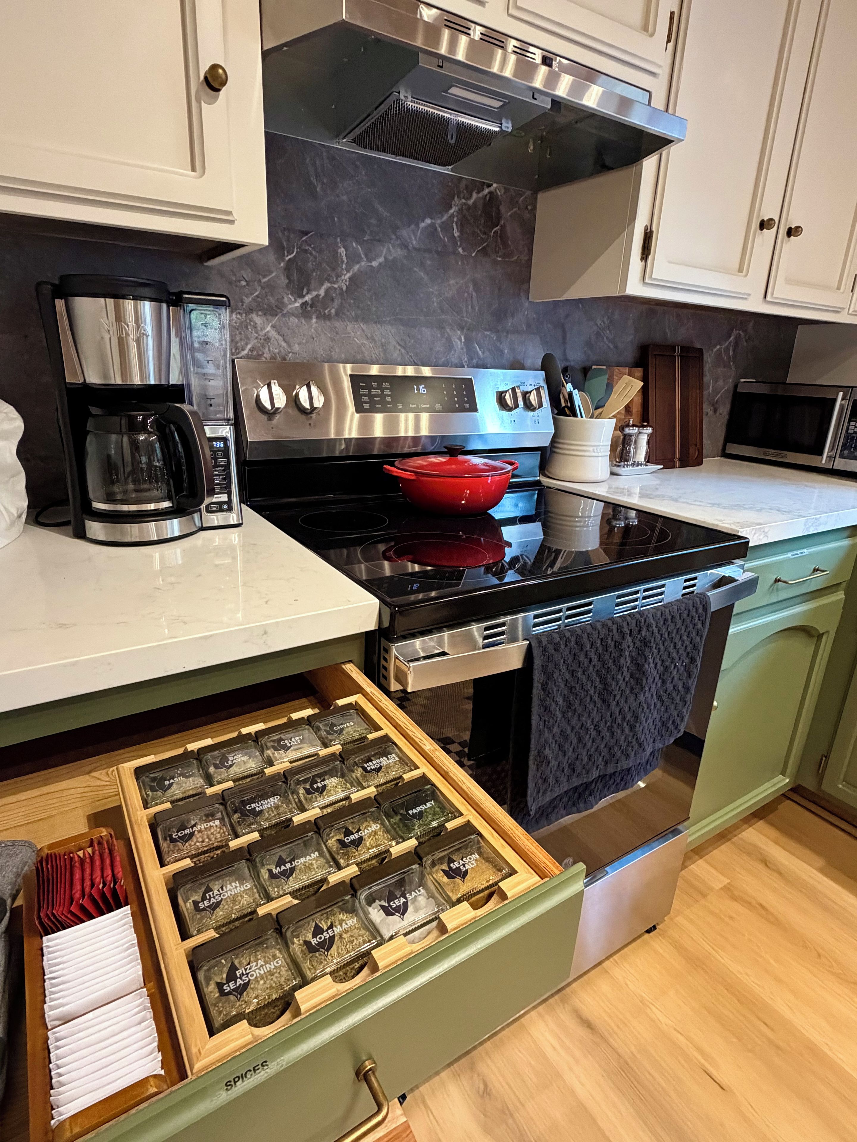 A kitchen with a stainless steel range, a red pot on the stove, a coffee maker, and a drawer of spices.