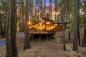 A cabin with a deck surrounded by trees, a clear sky, and a sunset. - Escape to Sequoia Grove Lodge! Modern 4BR/3BA BLS cabin with flat entry, new kitchen, game loft arcade, bunk room, and A/C. Walk 5 mins to private lake & golf; between Big Trees & Murphys. Perfect luxury retreat for multi-family & multi-gen groups! (Arnold)