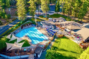 A large swimming pool with a sunshade, surrounded by a deck with lounge chairs, a small building with a balcony, and a parking area. - Escape to Sequoia Grove Lodge! Modern 4BR/3BA BLS cabin with flat entry, new kitchen, game loft arcade, bunk room, and A/C. Walk 5 mins to private lake & golf; between Big Trees & Murphys. Perfect luxury retreat for multi-family & multi-gen groups! (Arnold)