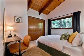 A bedroom with a bed, a desk, a chair, a window, and a door. - Escape to Sequoia Grove Lodge! Modern 4BR/3BA BLS cabin with flat entry, new kitchen, game loft arcade, bunk room, and A/C. Walk 5 mins to private lake & golf; between Big Trees & Murphys. Perfect luxury retreat for multi-family & multi-gen groups! (Arnold)