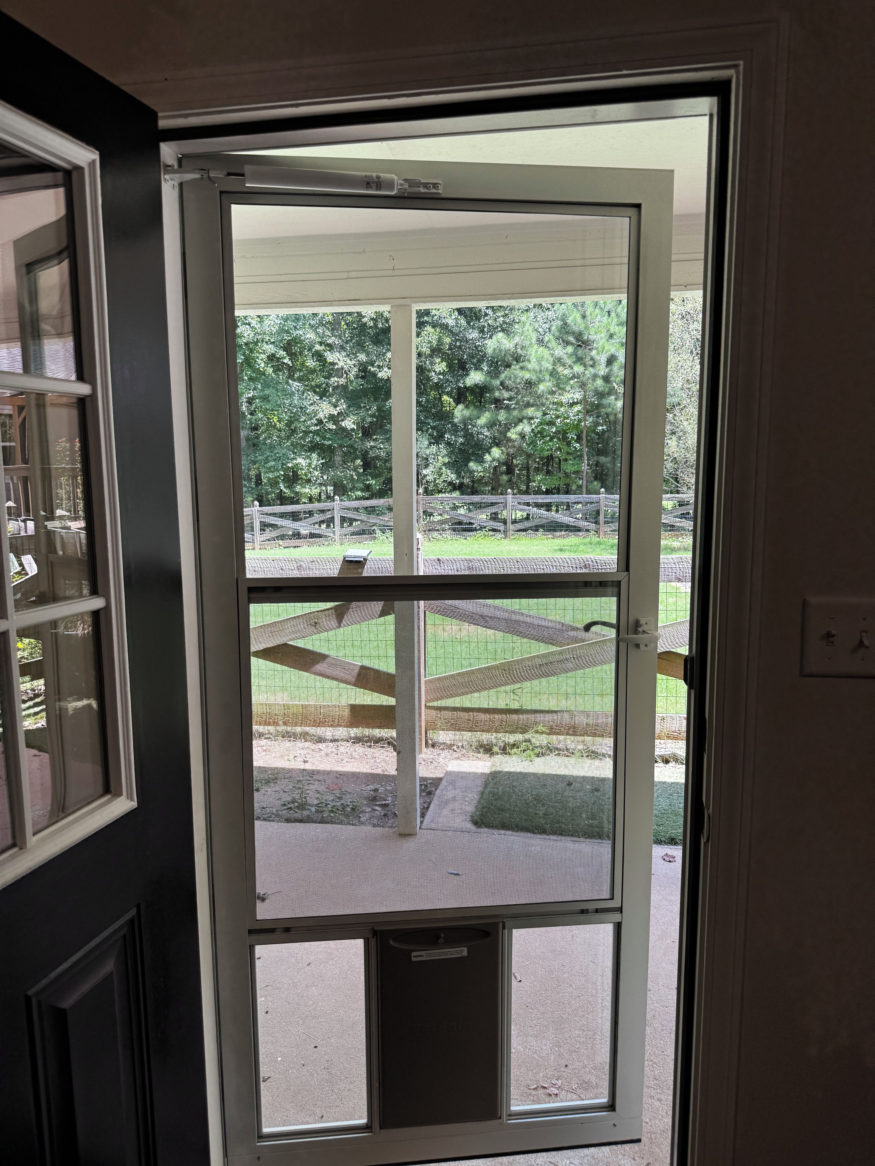 A door with a view of an outdoor area with a fence and greenery.