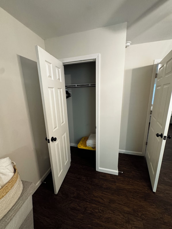 A room with a dark wooden floor, a white door, and a closet with a yellow storage bin.