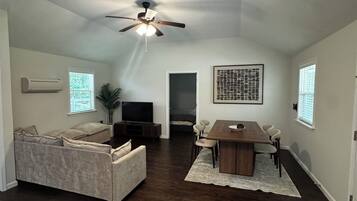 Amplia sala de estar con ventilador de techo, mesa de comedor con sillas, sofá y televisor.