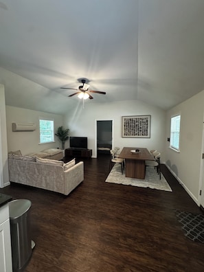 A spacious living area with a ceiling fan, a dining table with chairs, a sofa, and a TV.