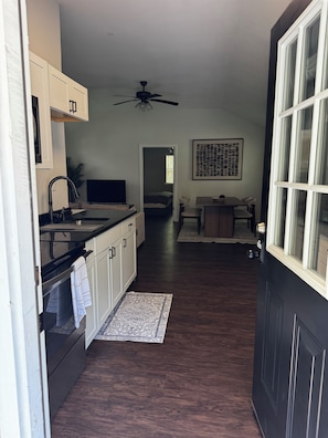 A narrow hallway with a kitchen on one side, a dining area with a table and chairs, and a bedroom with a bed in the distance.