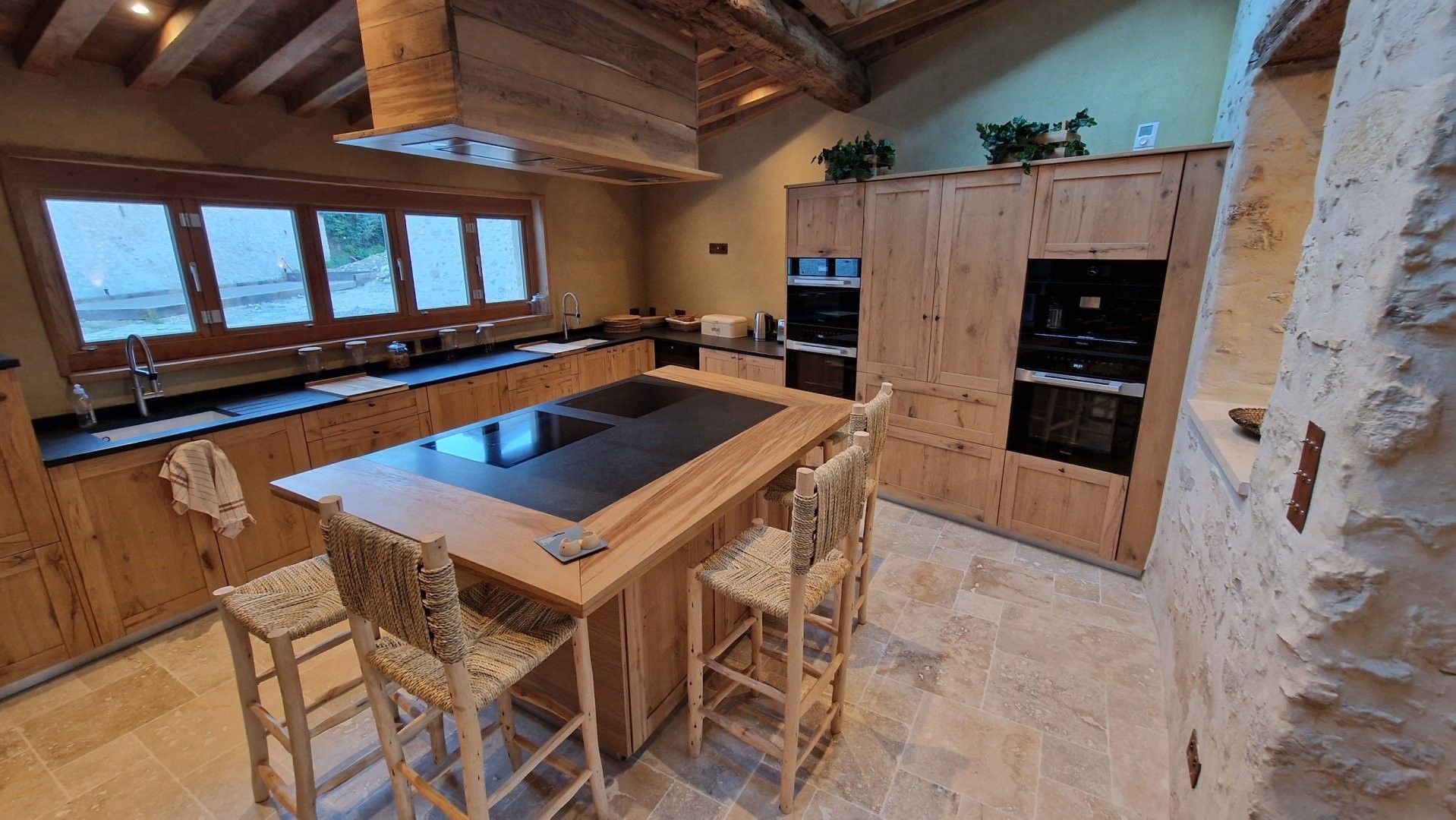 Une cuisine avec des meubles en bois, un îlot central et un mur en pierre.