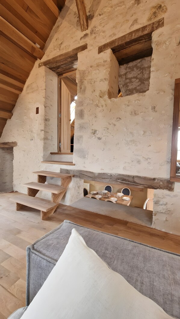 Ein rustikales Interieur mit einer Holztreppe, einem Essbereich mit Tisch für vier Personen und einer gemütlichen Sitzecke mit Kissen.