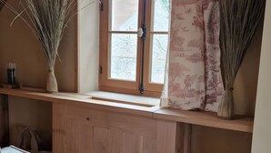 Una habitación acogedora con techo de madera, una ventana con cortina, un sofá y un jarrón con plantas secas.