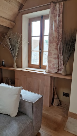 Ein gemütliches Zimmer mit Holzbalkendecke, einem Fenster mit Vorhang, einer Couch und einer Vase mit Trockenpflanzen.