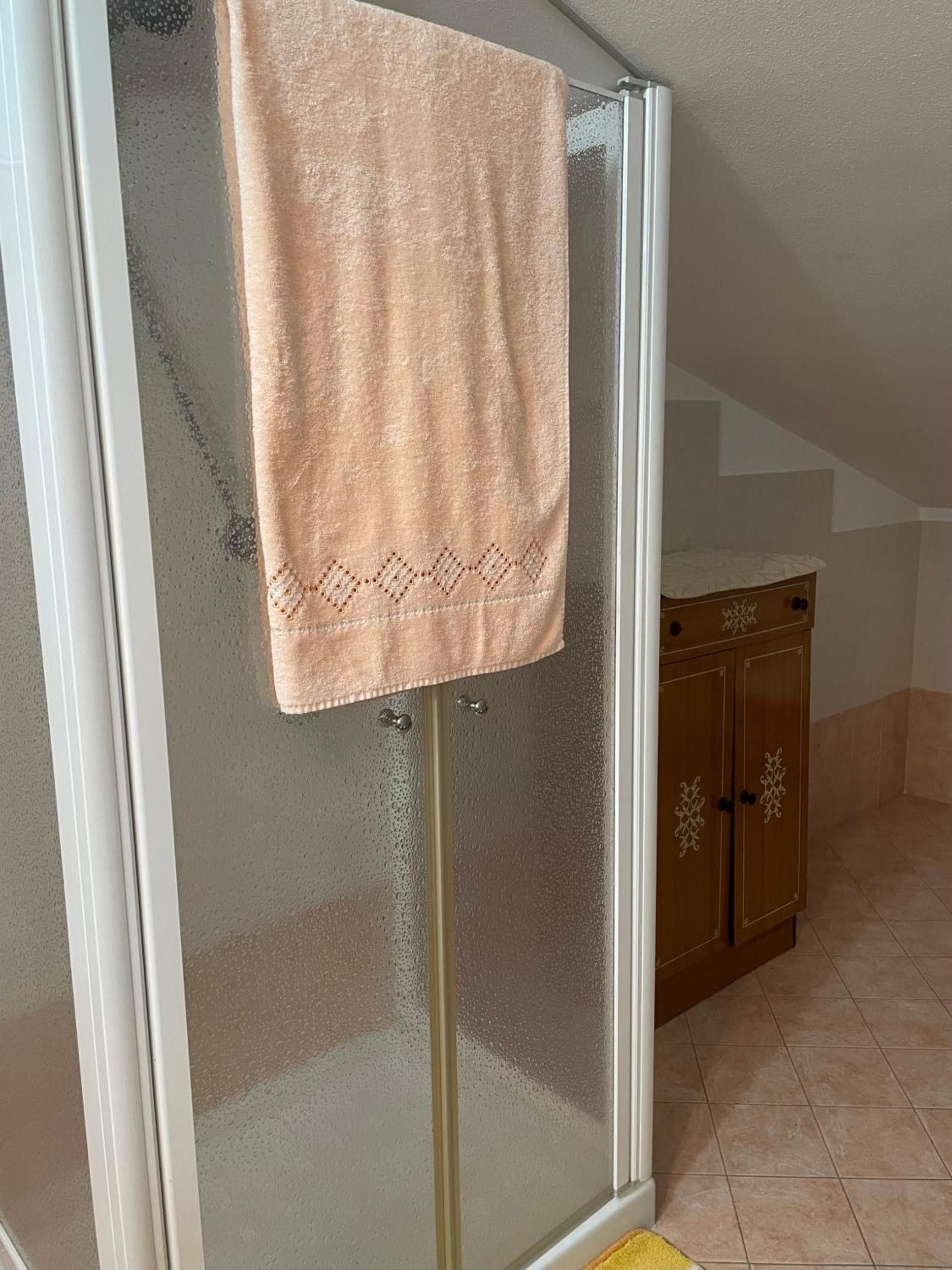 A bathroom with a glass shower door, a wooden cabinet, and a yellow bath mat.