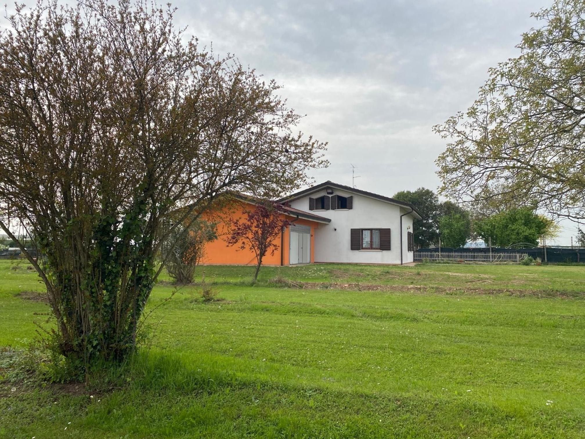 Casa de una planta con fachada blanca y sección anaranjada, rodeada de césped y árboles.