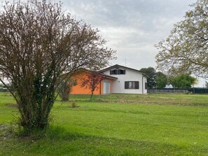 A single-story house with a white exterior and an orange section, surrounded by a grassy area and trees.