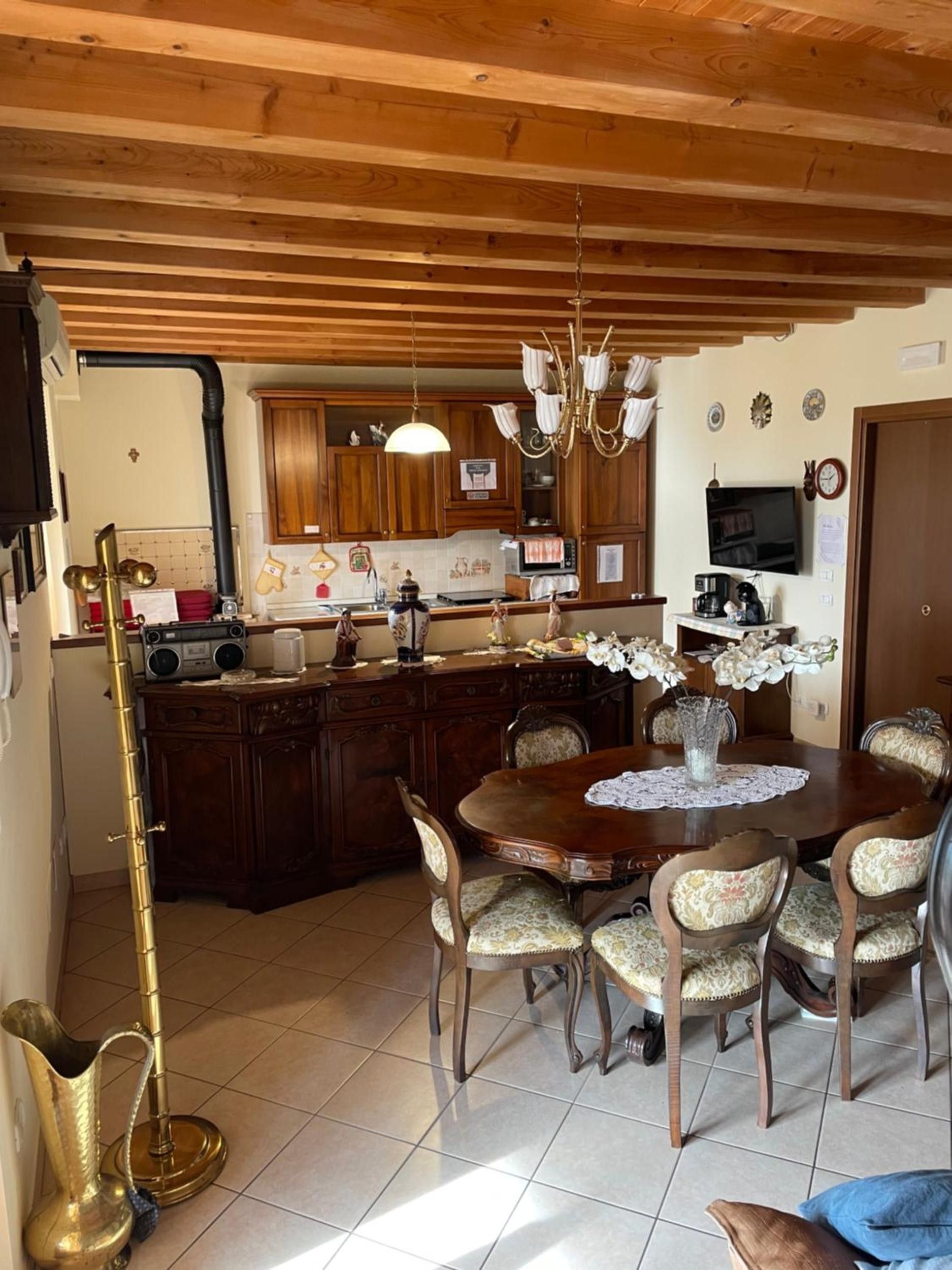 A dining area with a wooden table and chairs, a chandelier, and a kitchen in the background.