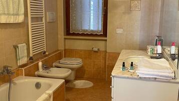 Un bagno con vasca, due servizi igienici, un lavandino e una finestra con tenda.