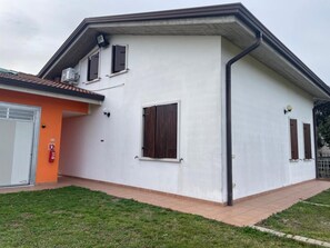Ein zweistöckiges Gebäude mit weißer Fassade, einem Ziegeldach und einem kleinen, angebauten orangen Bau.