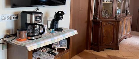 A living room with a flat-screen TV mounted on the wall, a coffee maker, a cabinet with drawers, and a wooden cabinet with glass doors.