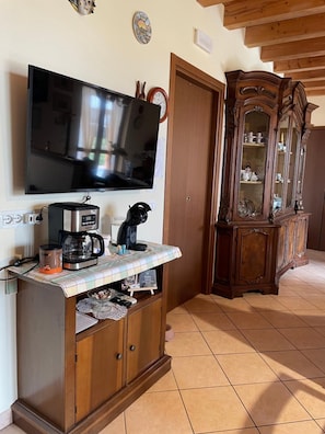 Un soggiorno con una TV a schermo piatto montata a parete, una macchina del caffè, un mobiletto con cassetti e un armadietto in legno con ante in vetro.