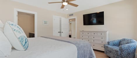 A bedroom with a bed, a ceiling fan, a television, a dresser, and a patterned chair.