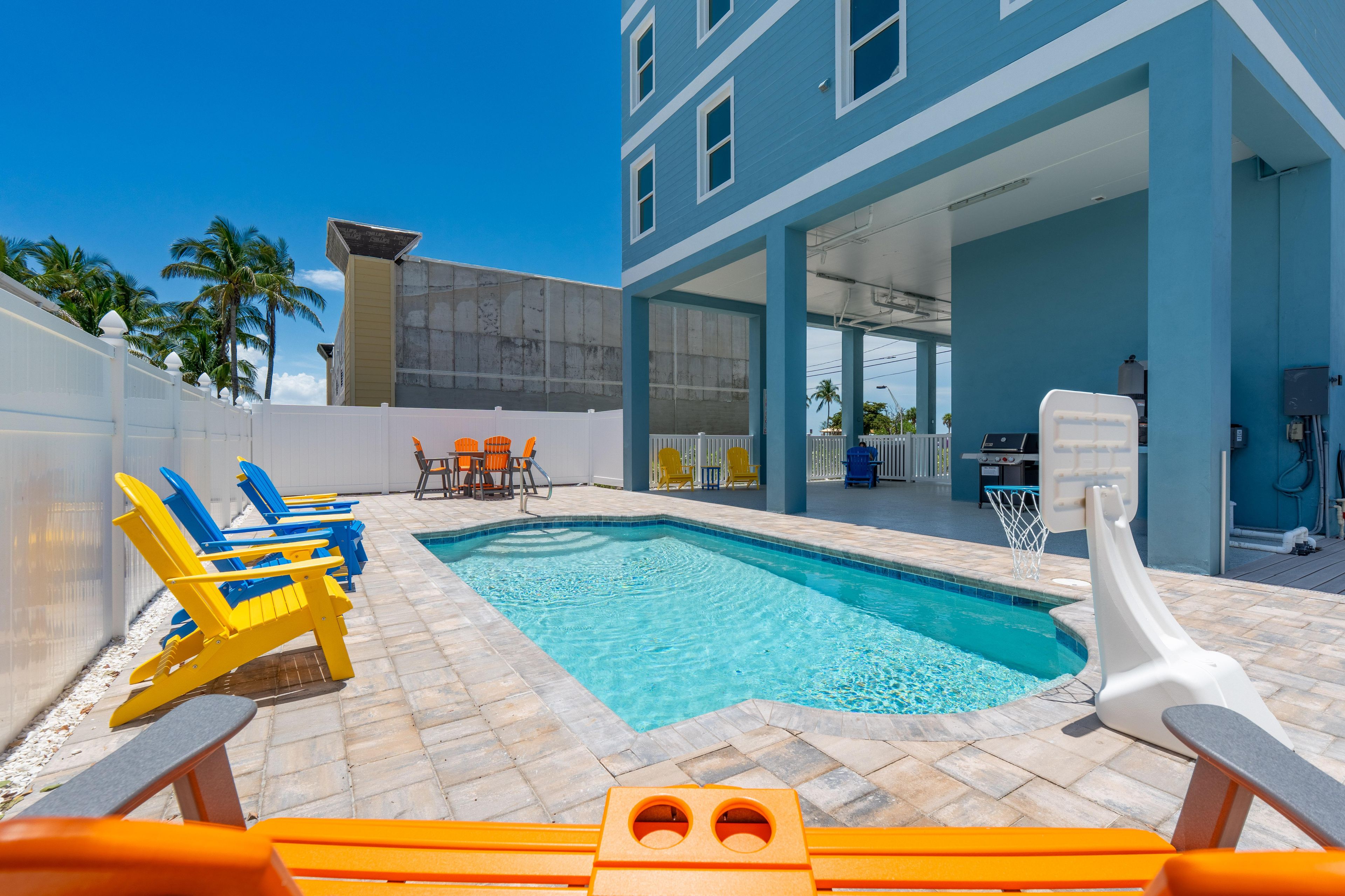 A swimming pool area with lounge chairs and a basketball hoop.