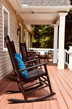 Eine Veranda mit Holzboden, weißer Geländer und zwei Schaukelstühlen mit Kissen.