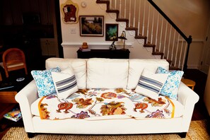 Un salon avec un canapé blanc, un plaid à motifs et un escalier en arrière-plan.