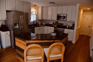 A kitchen with white cabinets, a stainless steel refrigerator, a microwave, and a wooden island with two wicker chairs. - Escape to beautiful Lake Anna in this spacious amenity loaded retreat! (Mineral)